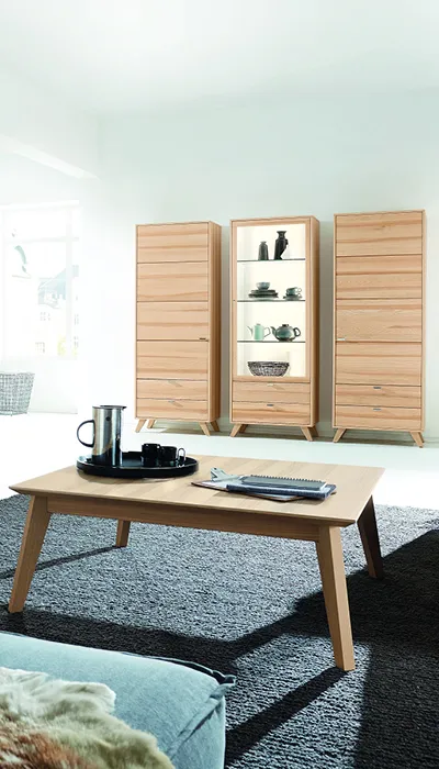 Moderner Wohnraum mit drei hohen Vitrinenschränken aus Massivholz, beleuchteter Glaseinlage und passendem Holzcouchtisch, eingerichtet im hellen, minimalistischen Stil mit viel Tageslicht.